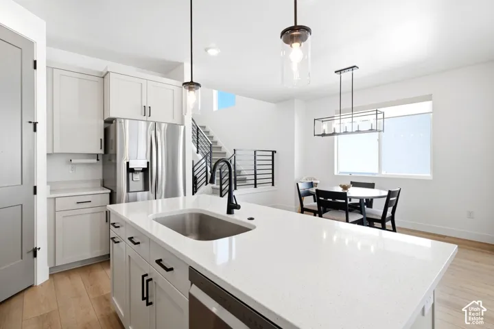 Kitchen featuring a white countertop island with an undermount sink, stainless steel appliances, white cabinetry, and wood-finish flooring