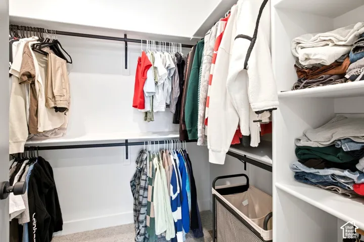 Walk-in closet featuring white built-in shelving, multiple hanging rods, and light-toned carpeting