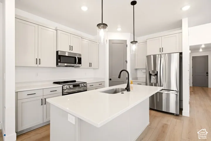 Kitchen featuring shaker-style cabinetry, a central island with a quartz countertop, stainless steel appliances, matte black hardware, and wood-finish flooring