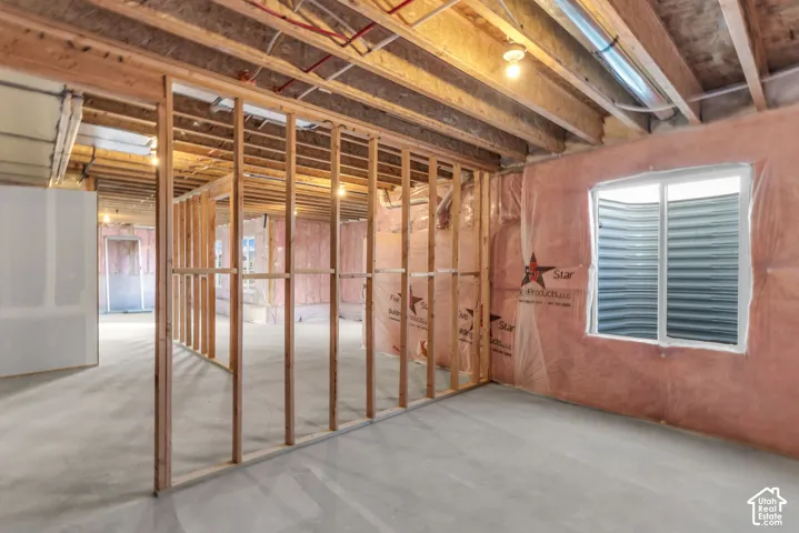 Unfinished basement  bedroom with exposed wood framing, concrete flooring, and an egress window from the basement.