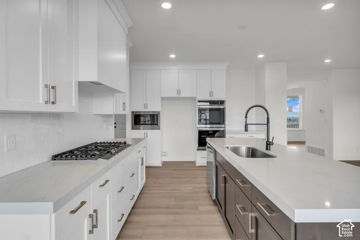 Kitchen featuring white shaker-style cabinetry, a gas cooktop with a matching range hood, stainless steel appliances, a center island with an undermount sink.