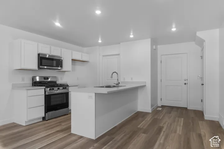 Kitchen featuring white cabinetry, stainless steel appliances, light-toned countertops, and wood-finish flooring