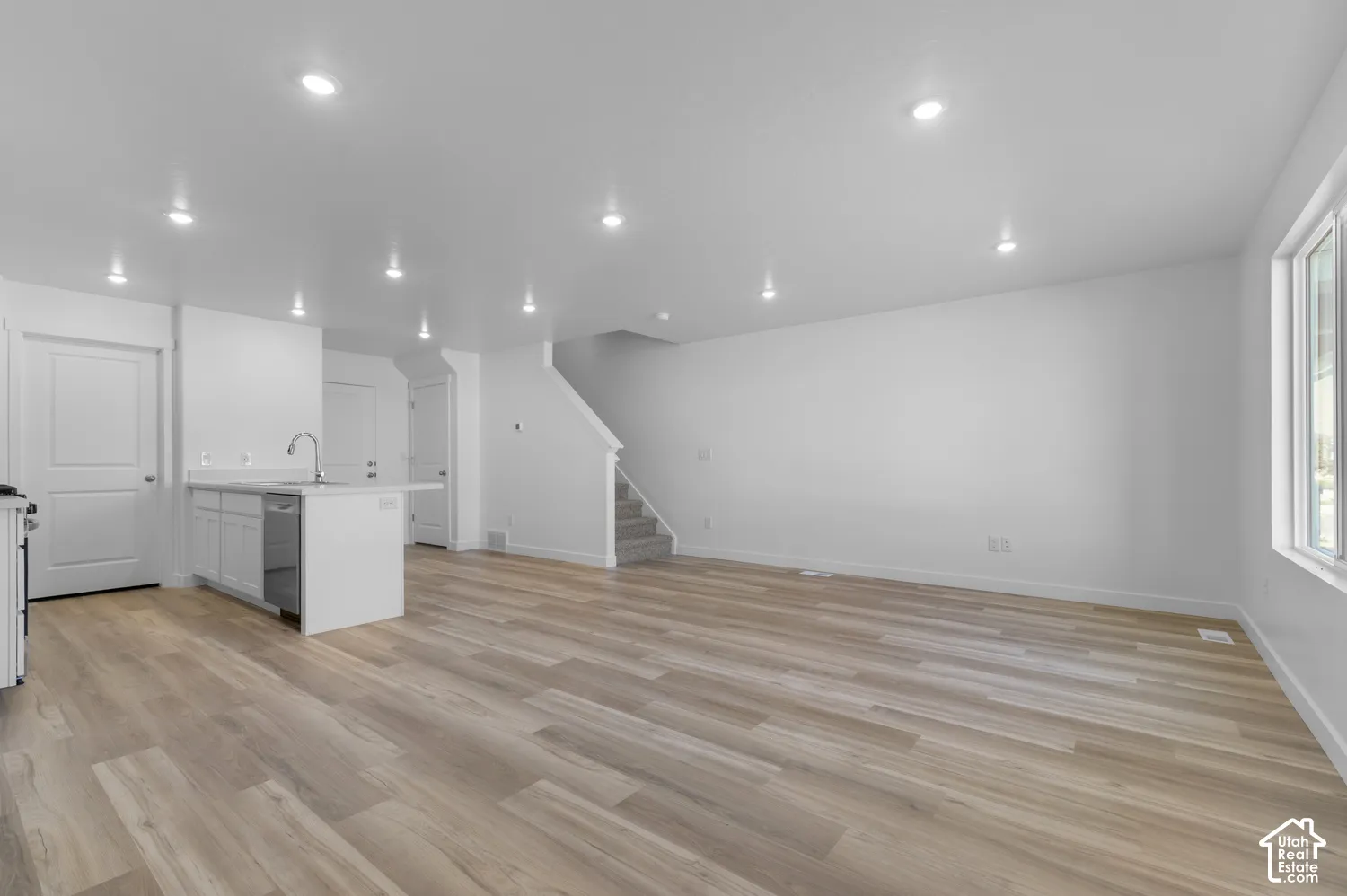 Open-concept living space featuring wood-finish flooring, recessed lighting, and a white kitchen island with an integrated sink