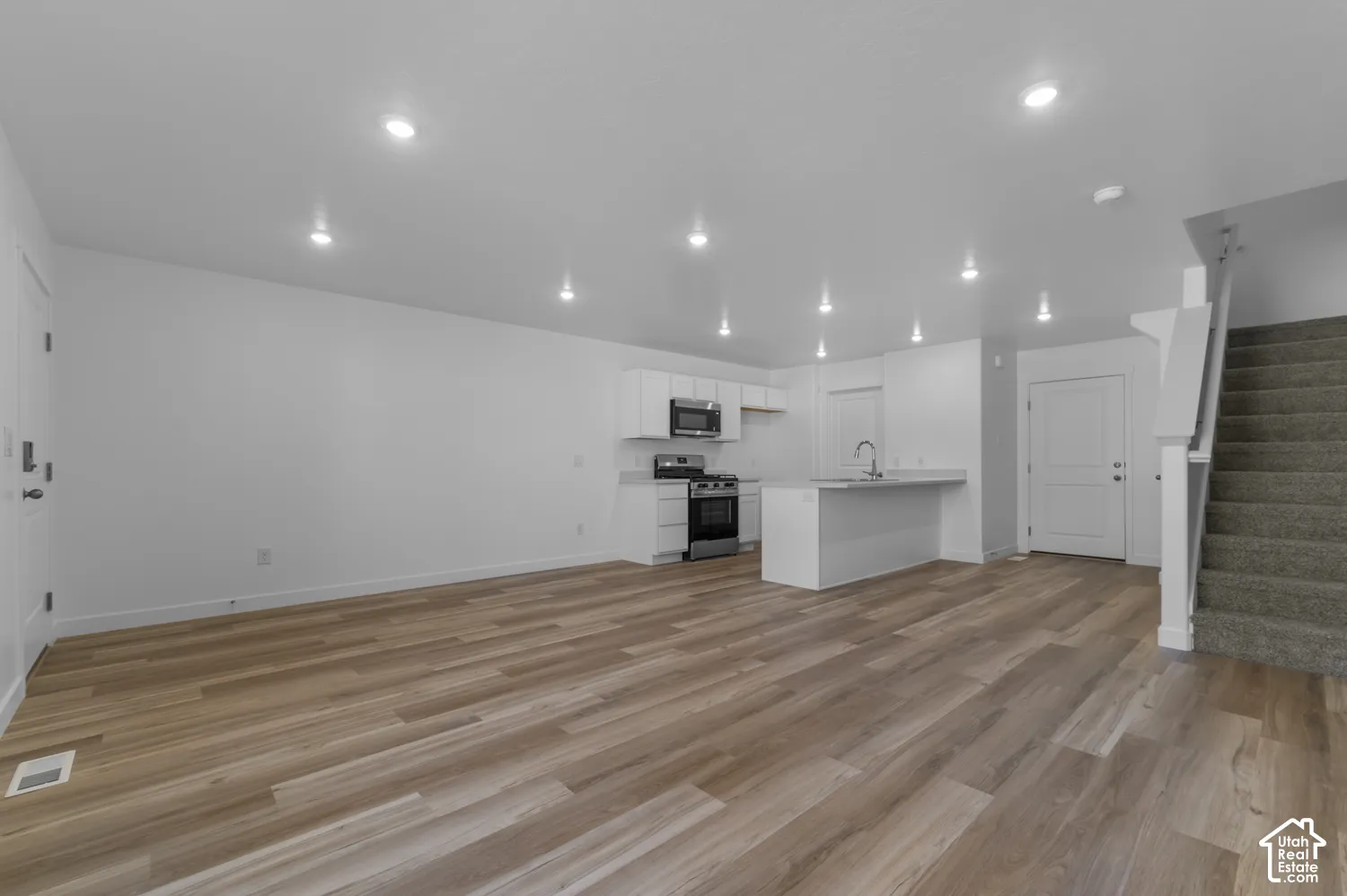 Open concept living space featuring wood-finish flooring, recessed lighting, and a modern kitchen with white cabinetry
