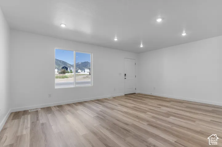 Wood-finish flooring, recessed lighting, white interior walls, white paneled door, and a large window