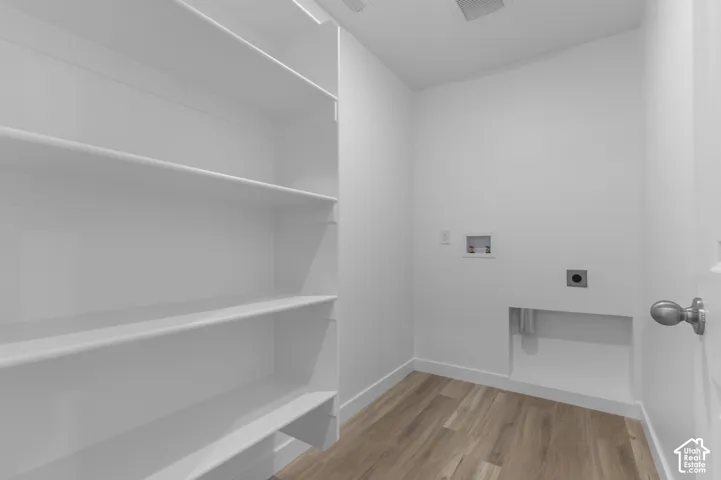 Laundry area featuring integrated shelving, wood-finish flooring, and white walls