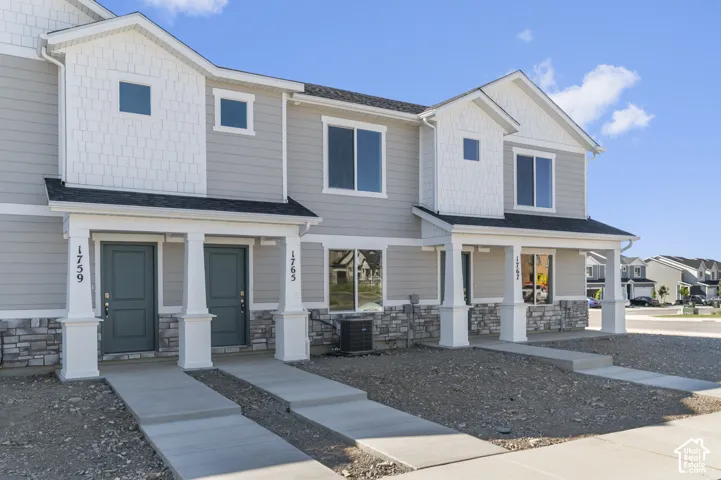 Two-story exterior with light gray siding, white shake accents, stone veneer foundation, and a covered entry
