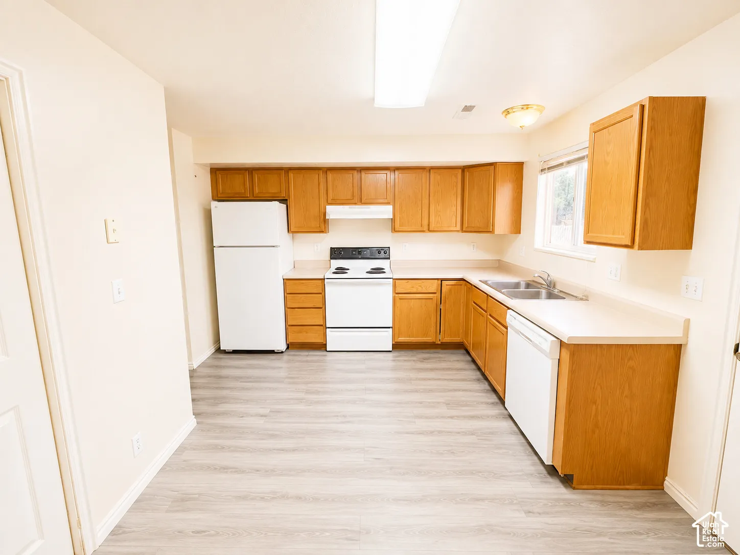Spacious kitchen featuring wood-finish cabinetry, white appliances including refrigerator and electric range, laminate countertops, stainless steel sink, and wood-finish flooring throughout