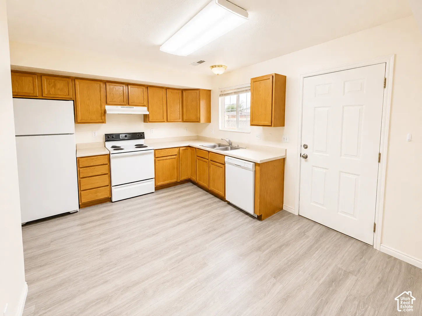 Spacious kitchen featuring wood cabinetry, white appliances including a refrigerator, electric range, and dishwasher, laminate countertops, a large sink, and wood-finish flooring throughout