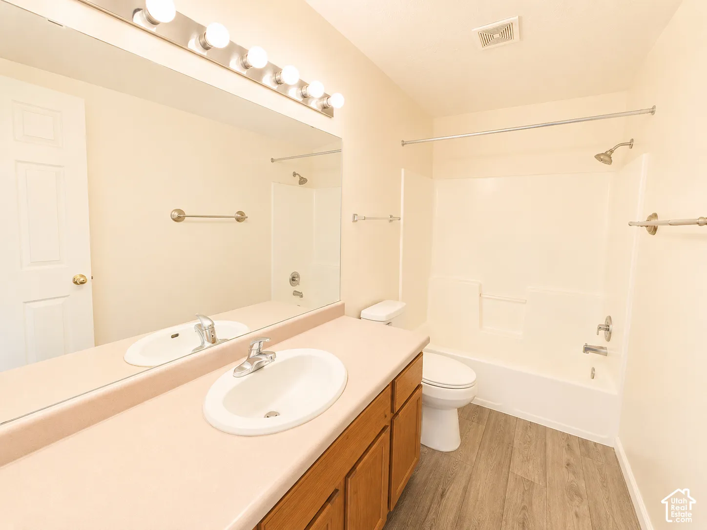 Wood-finish flooring with a vanity featuring a double sink, a full-width mirror, and a built-in shower/tub combination
