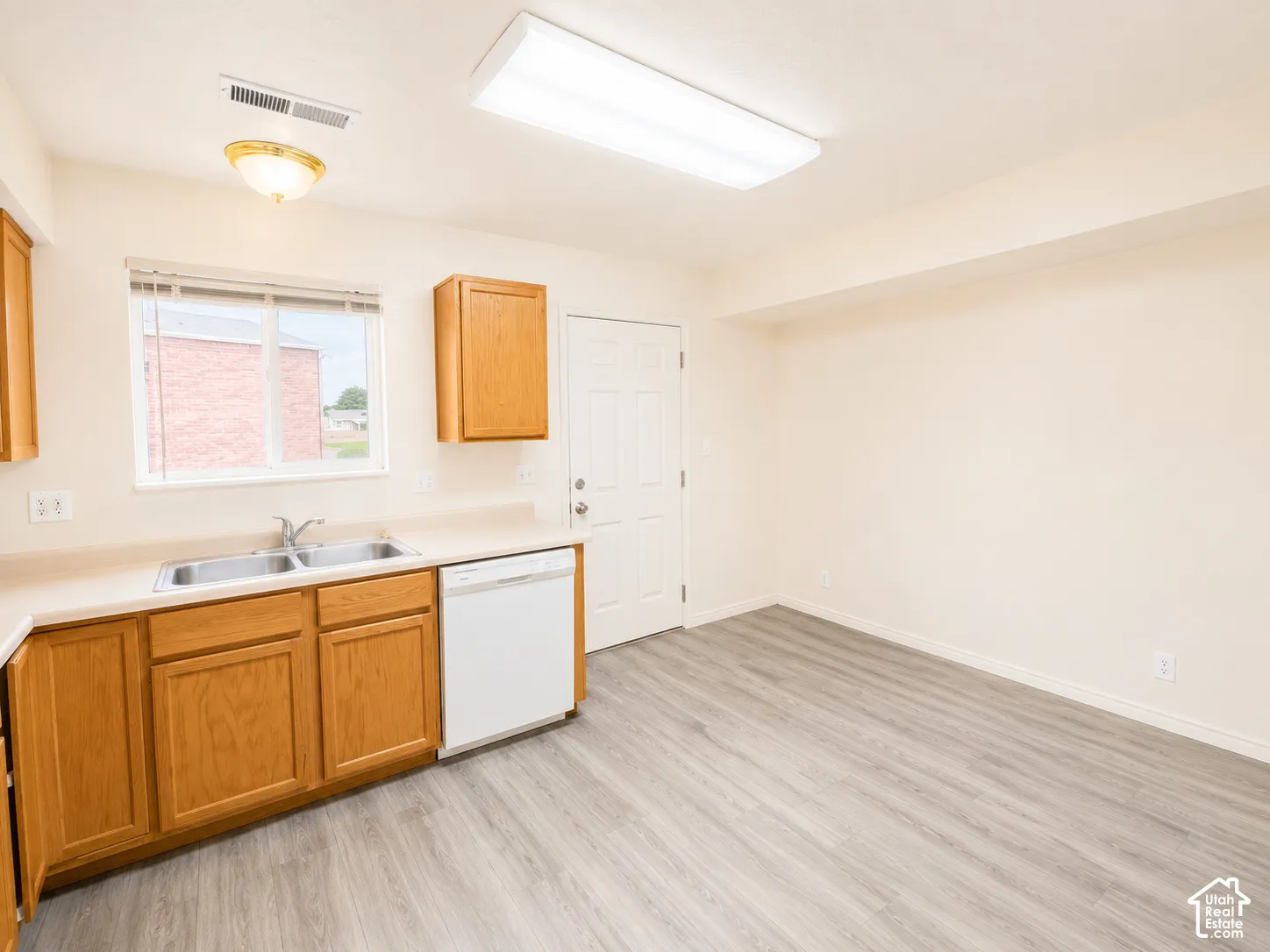 Bright utility kitchen featuring wood-finish cabinetry, white appliances, stainless steel sink, and ample counter space