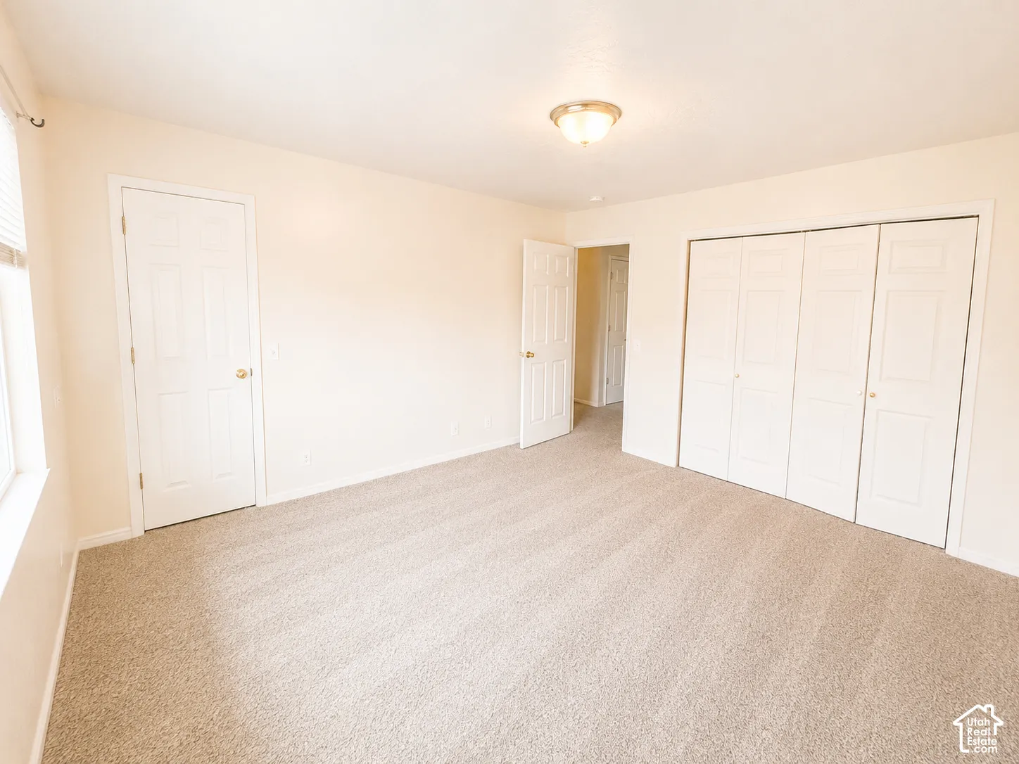 Soft neutral carpeting, window with blinds, ceiling-mounted light fixture, and bi-fold closet doors