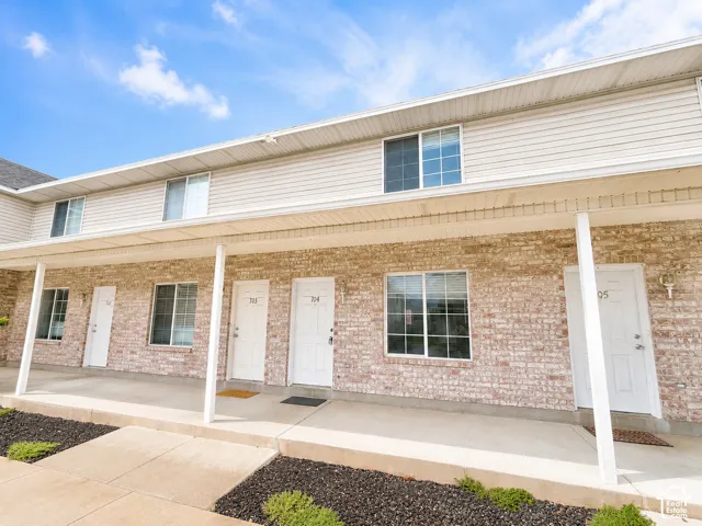 Brick facade with light-colored siding, covered entryway, multiple windows, and individual unit entrances