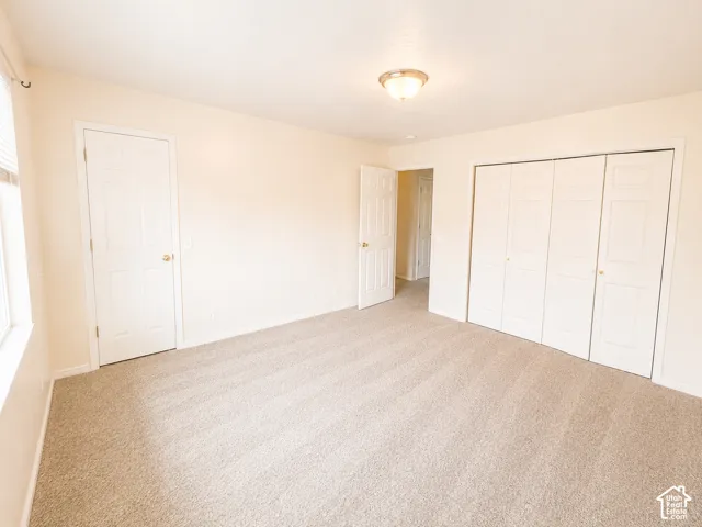 Soft neutral carpeting, window with blinds, ceiling-mounted light fixture, and bi-fold closet doors