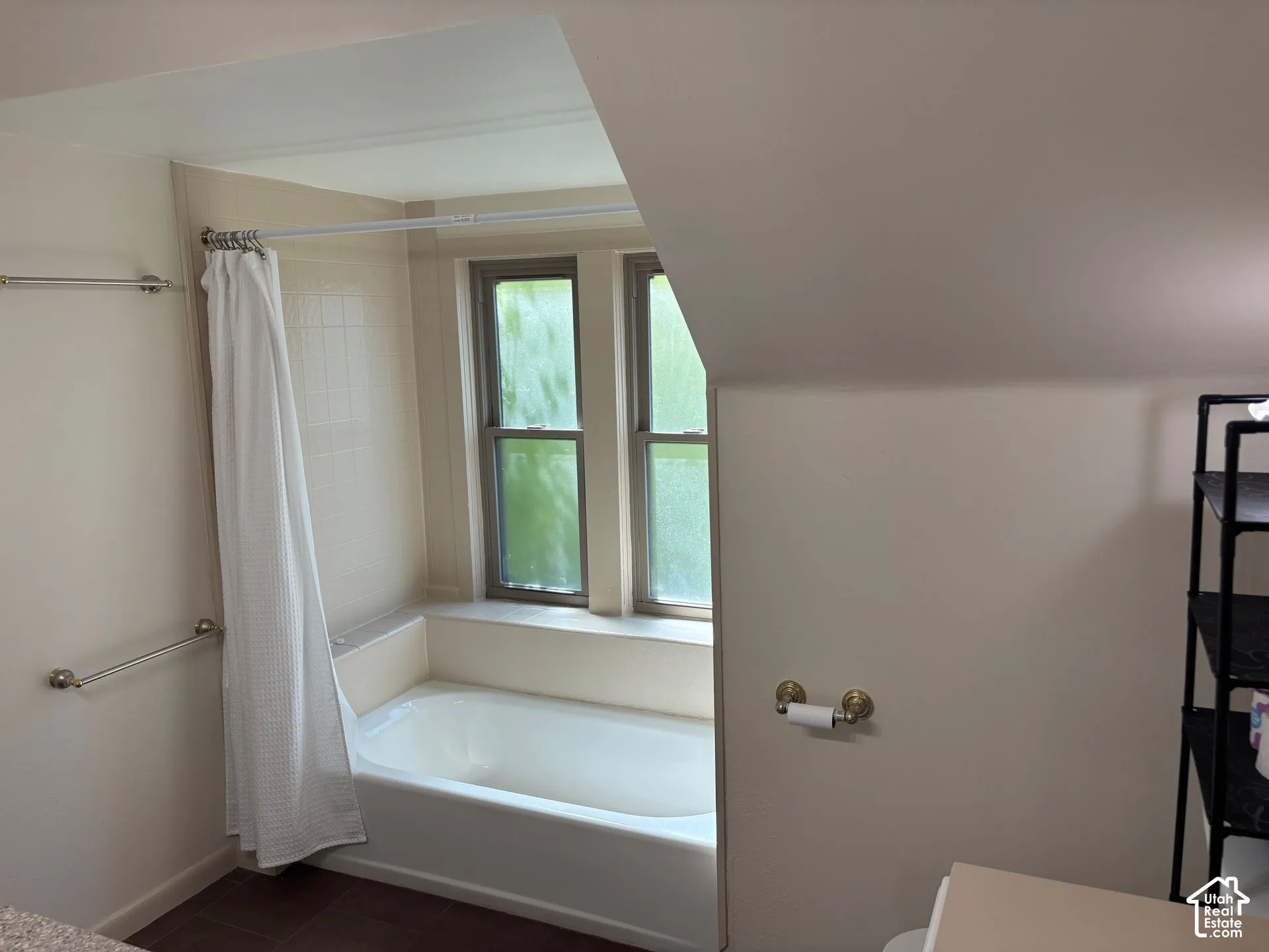 Bathtub with tiled surround, dual windows, and wood-finish flooring