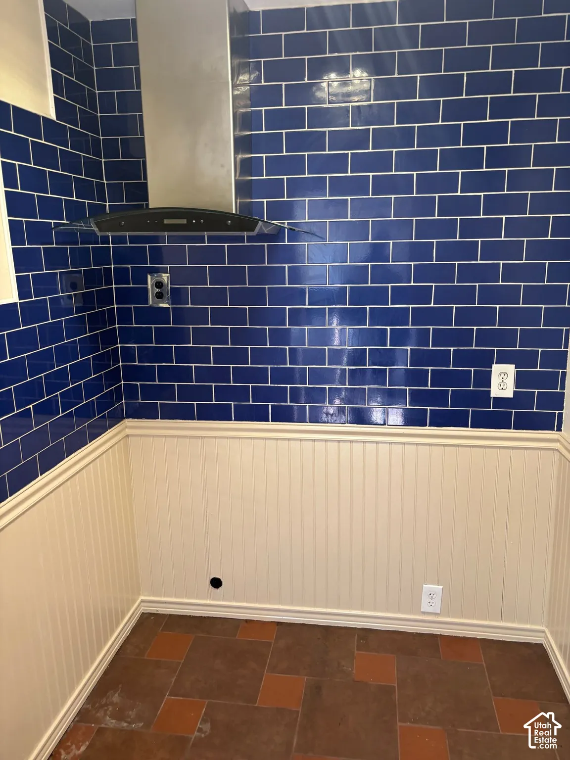 Stainless steel range hood, blue subway tile, beadboard wainscoting, decorative trim, and multi-toned floor tile