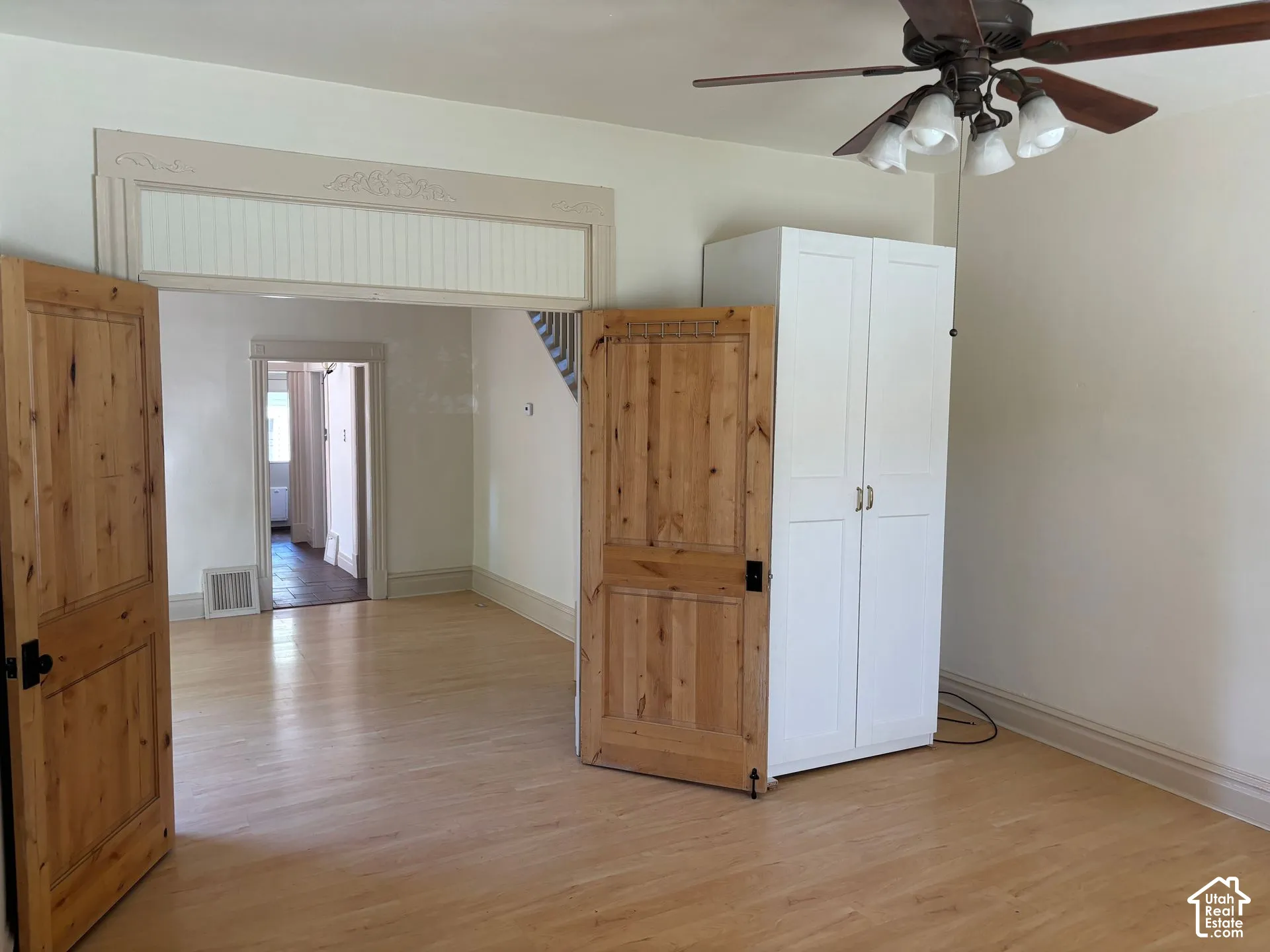 Light wood-finish flooring, a ceiling fan with light fixture, and natural wood doors