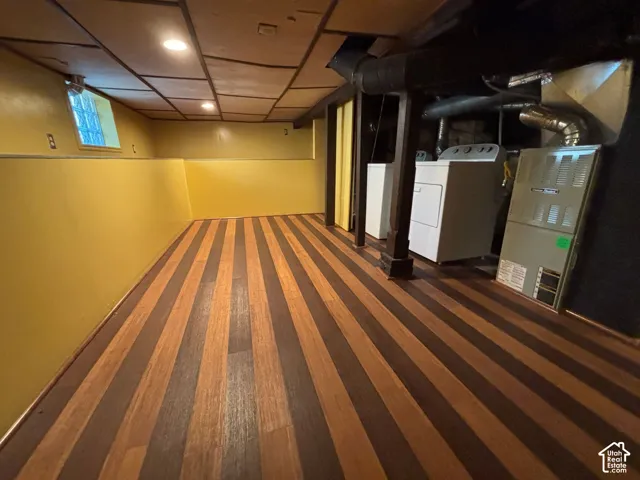 Wood-finish flooring, drop ceiling with recessed lighting, and a utility area featuring a washer, dryer, and furnace
