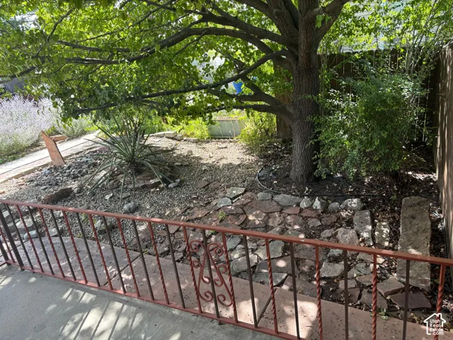 Expansive outdoor area featuring mature trees, diverse plantings, natural stone hardscaping, and a decorative wrought iron railing