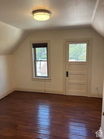 Wood-finish flooring, single window, flush mount ceiling light fixture, paneled interior door, and sloped ceiling