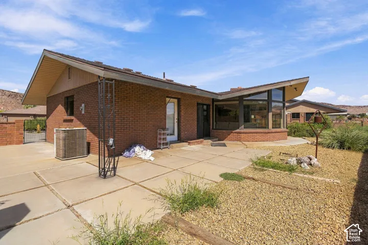 Brick exterior with multiple roof lines, expansive concrete patio, large picture windows, and gravel landscaping
