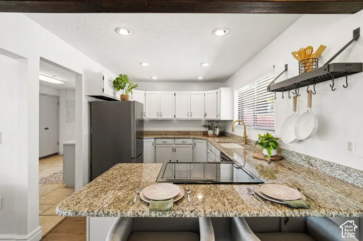 Kitchen featuring an electric cooktop, light-toned cabinetry, speckled countertops, a gold-toned faucet, and recessed lighting