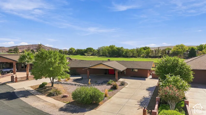 Brick exterior with an extended covered entry, concrete driveway, and mature landscaping