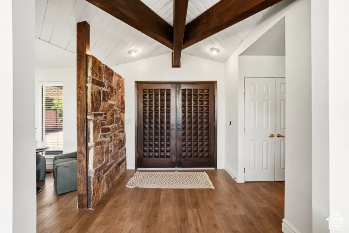 Vaulted wood-paneled ceiling with exposed wood beams, wood-finish flooring, stone accent wall, and decorative double entry doors