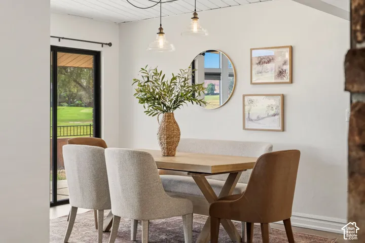 Dining area with a natural wood-finish table, white planked ceiling, and two glass pendant light fixtures