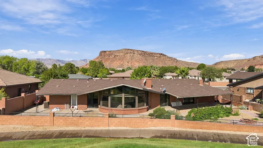 Single-story brick exterior, extensive rear patio, substantial fixed glass windows, prominent rock formations, and mature foliage