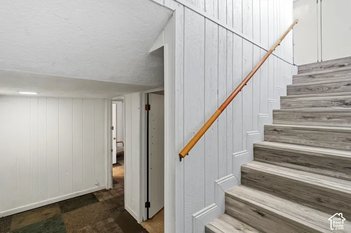 Staircase featuring wood-finish treads and risers, a wood handrail, and white paneled walls