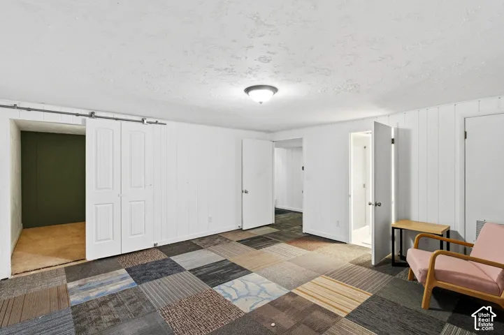 Room featuring paneled walls, ceiling-mounted light fixture, and multi-patterned carpet squares