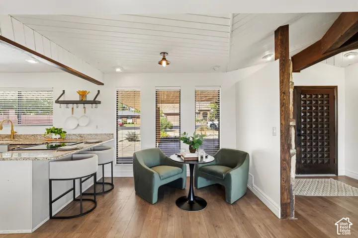 Wood-finish flooring throughout, vaulted planked ceiling, three large windows with blinds, granite countertop with breakfast bar, and a patterned entry door