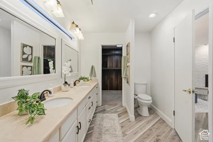 Dual vanity with undermount sinks and dark bronze fixtures, light-toned countertop, wood-finish flooring in a herringbone pattern, and recessed lighting