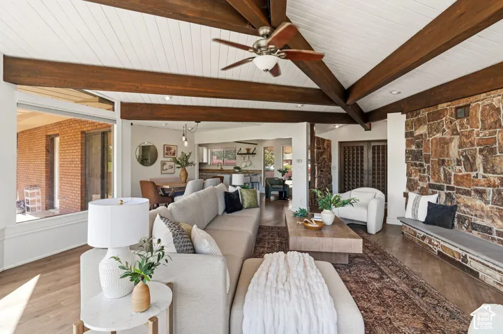 Vaulted ceiling with exposed wood beams, stone accent wall with built-in stone bench, wood-finish flooring, and large picture windows