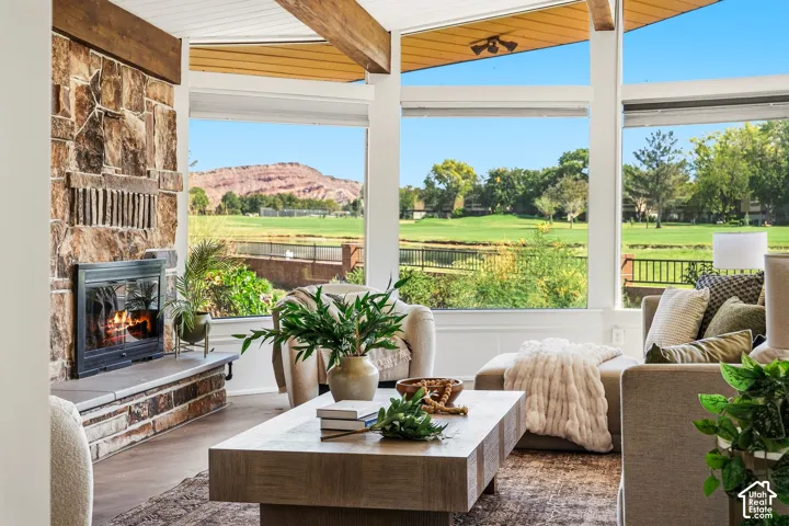 Vaulted ceiling with exposed wood beams, stone-clad fireplace, large windows, wood-finish flooring, and a golf course backdrop