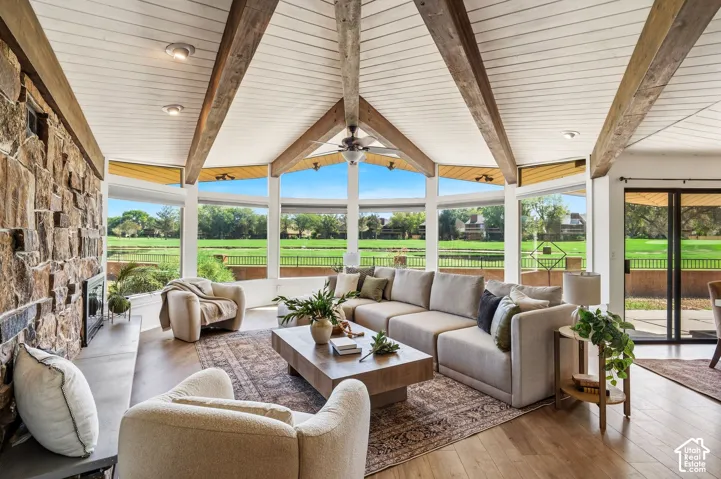 Vaulted ceiling with exposed wood beams, stone-clad fireplace, wood-finish flooring, full-height windows, and sliding glass doors