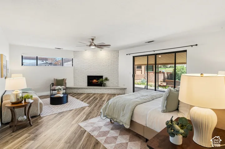 Wood-finish flooring, white brick fireplace with hearth, ceiling fan, and sliding glass door leading to outdoor space