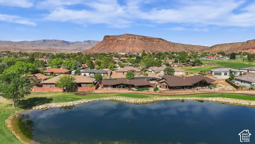 Waterfront property with a lush green perimeter, adjacent to a residential area, set against a mountainous backdrop