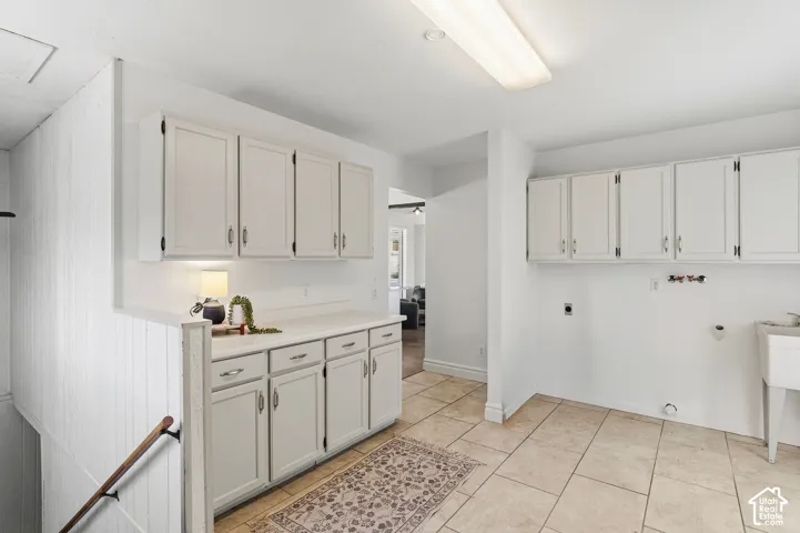 White cabinetry, tile flooring, built-in utility sink, and wall-mounted lighting