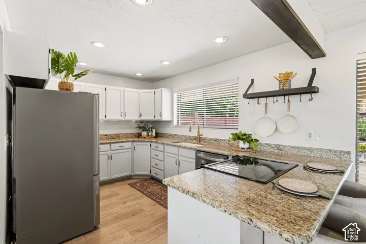 L-shaped kitchen featuring white cabinetry, granite countertops, an integrated cooktop, a built-in stainless steel refrigerator, and recessed lighting