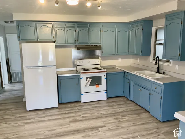 Kitchen featuring blue cabinetry, light-toned countertops, a white refrigerator, a white range, and wood-finish flooring