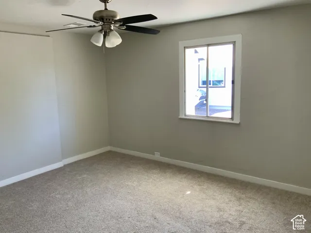 Neutral tone wall paint, carpeted flooring, window with white trim, and a ceiling fan with integrated lighting