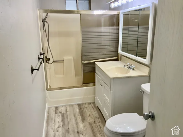 Contemporary bathroom featuring a vanity with ample storage and countertop space, a ceramic sink with chrome fixtures, a separate toilet, wood-finish flooring, and an enclosed shower with glass enclosure and overhead showerhead