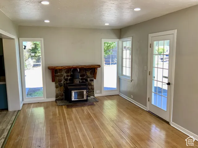 Hardwood flooring, recessed lighting, stone-clad fireplace with wood stove, and multiple windows