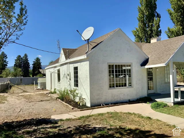 Stucco exterior with a pitched roof, featuring a covered porch, multiple windows, and a concrete pathway