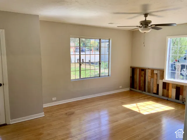 Wood-finish flooring, multiple windows, ceiling fan, and decorative wood paneling