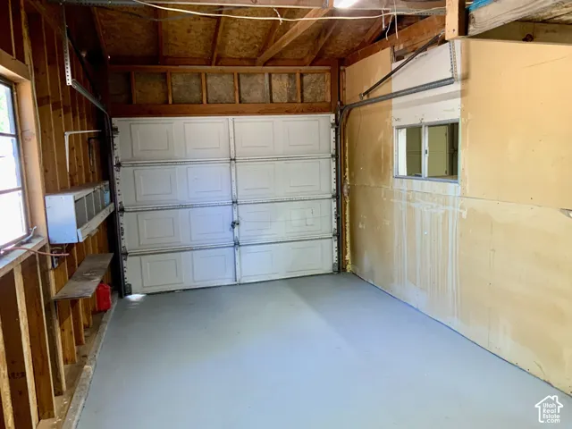 Spacious garage featuring an overhead sectional door, finished flooring, wood-beam ceiling structure, and natural lighting from side windows