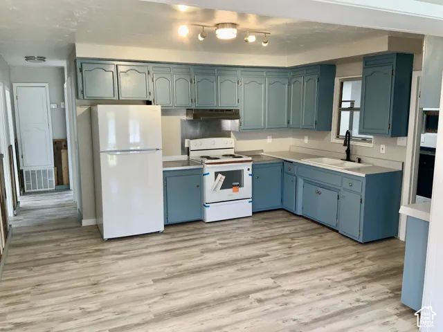 Kitchen featuring painted cabinetry, light-toned countertops, a stainless steel sink with a black faucet, and wood-finish flooring