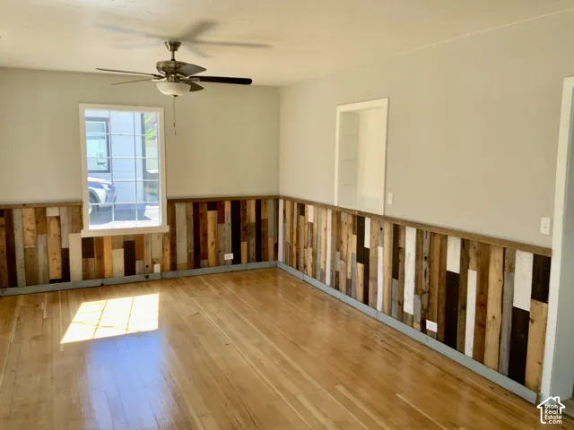 Hardwood flooring, multi-tone wood paneling, ceiling fan with integrated lighting, and a window with white grid inserts